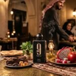 Foto de estúdio do frasco de perfume "9 pm Night Out" da Afnan, cercado por madeira, pitaya, maçã e hortelã sob iluminação quente.