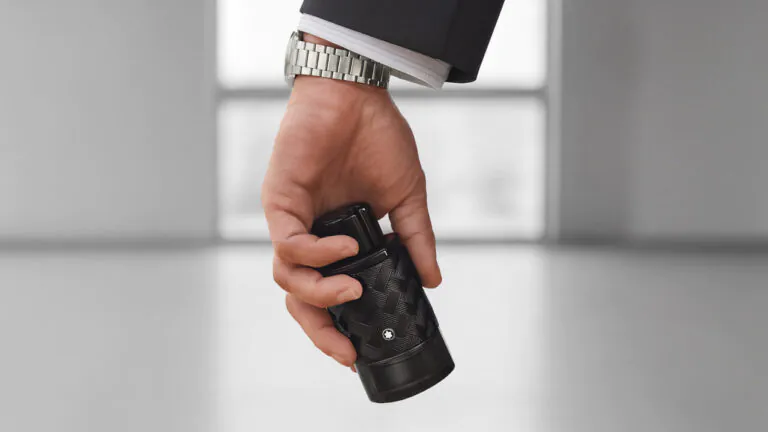 Uma mão masculina segurando o frasco do perfume Montblanc Explorer Extreme em um ambiente moderno e minimalista.