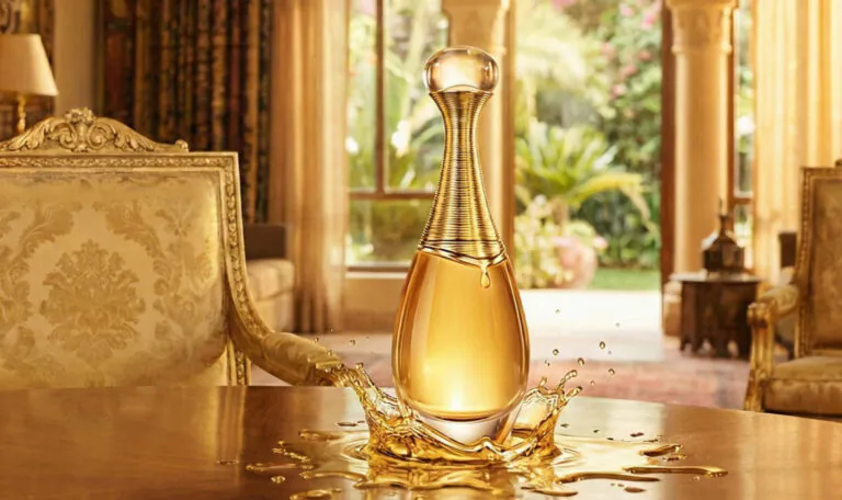 Frasco de perfume Dior J'adore sobre uma mesa de madeira polida, emergindo de um respingo dourado de líquido. O cenário é uma sala luxuosa com decoração em tons quentes, tapeçarias ricas e luz solar entrando por janelas em arco.