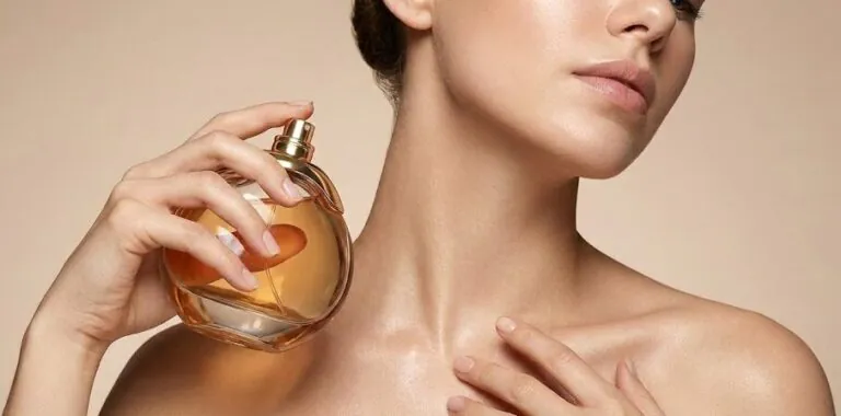 Mulher de pele iluminada aplicando perfume no pescoço, ilustrando a busca por fragrâncias de alta fixação.